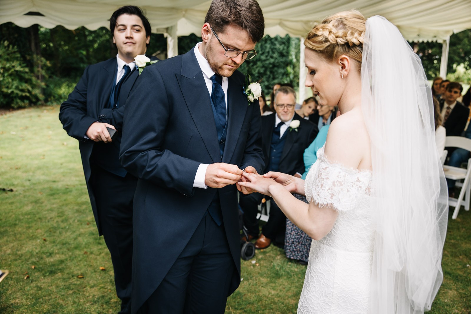 The groom sliding the ring onto the bride's finger, the best man alongside