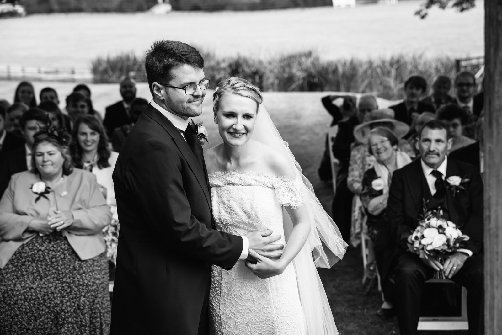 Black-and-white of the newlyweds embracing as guests applaud behind