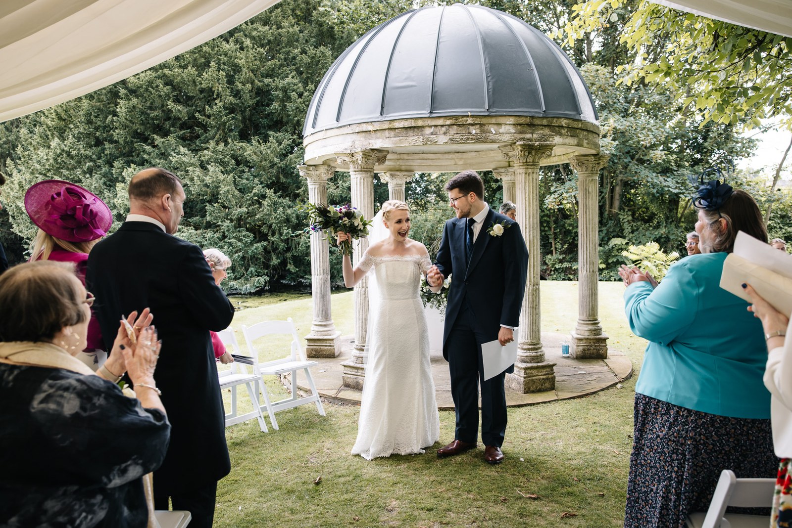 The couple standing together at the temple while guests clap and cheer