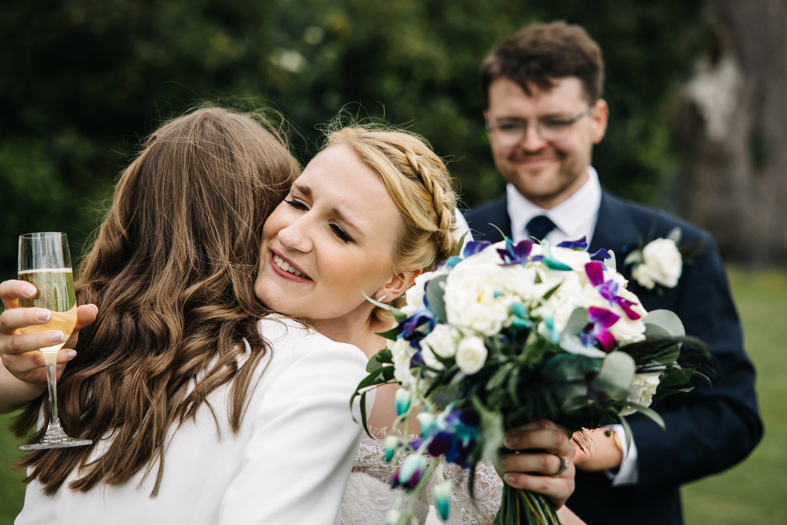 The bride hugging a guest while the groom holds her bouquet