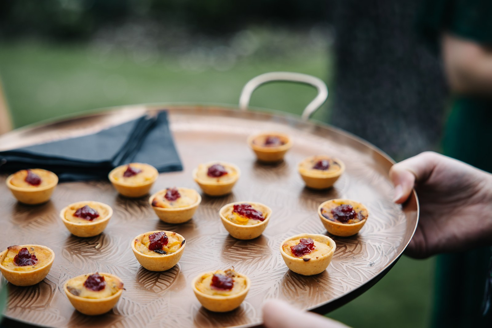 A tray of canape tartlets topped with red relish carried by a server