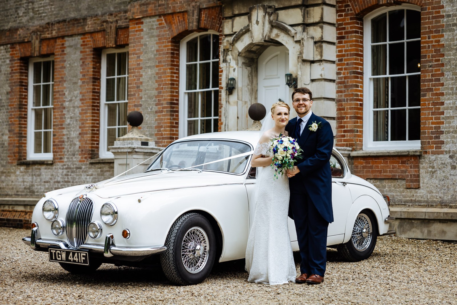 The couple posing beside a vintage white Jaguar outside Ardington House