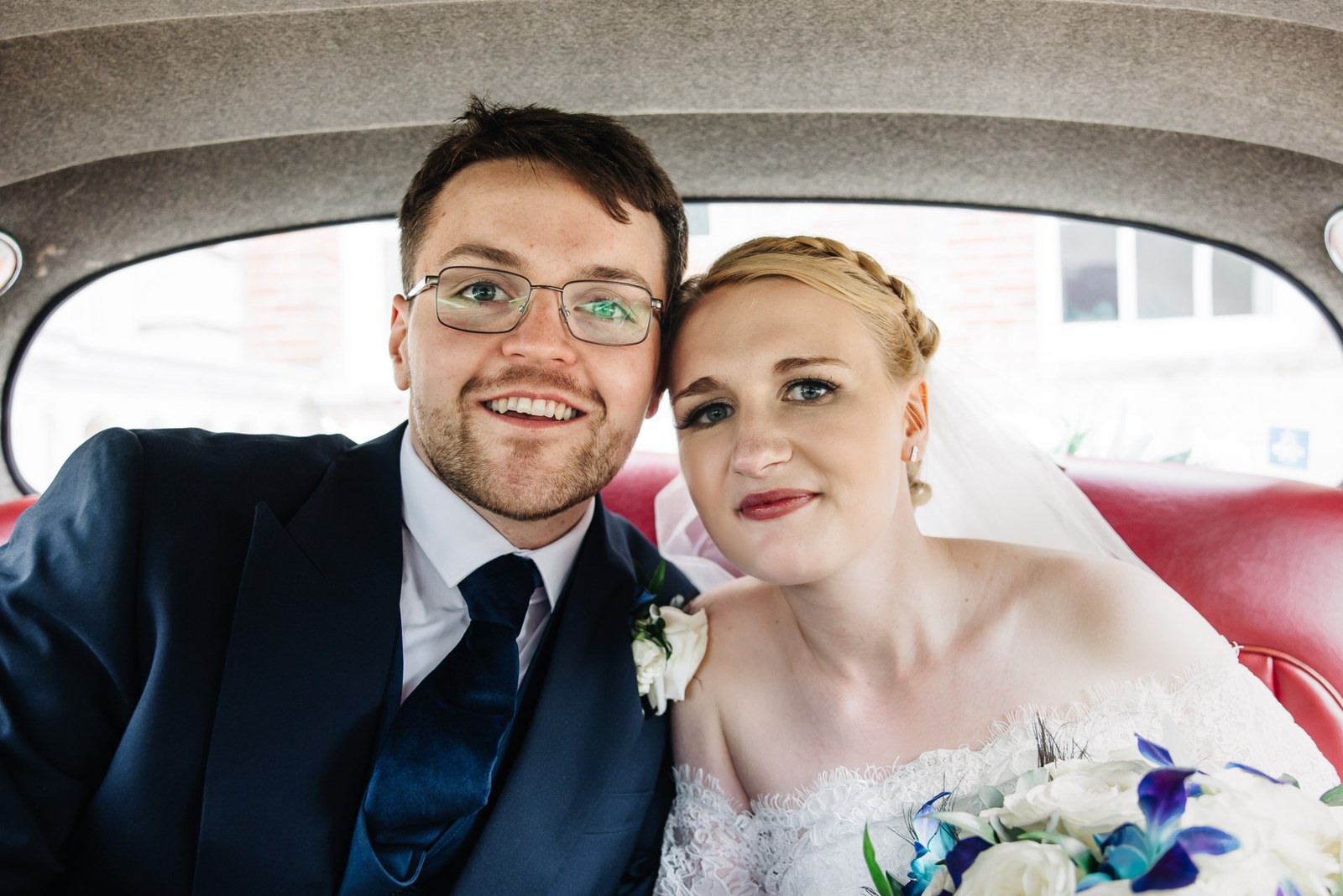 The newlyweds side by side in the back seat of the classic car