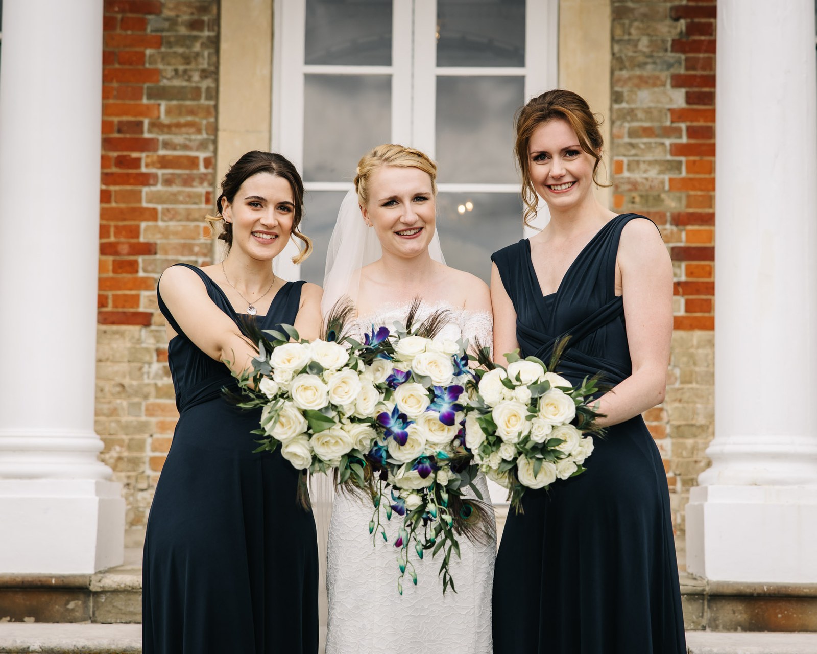 The bride flanked by two bridesmaids in navy holding white bouquets