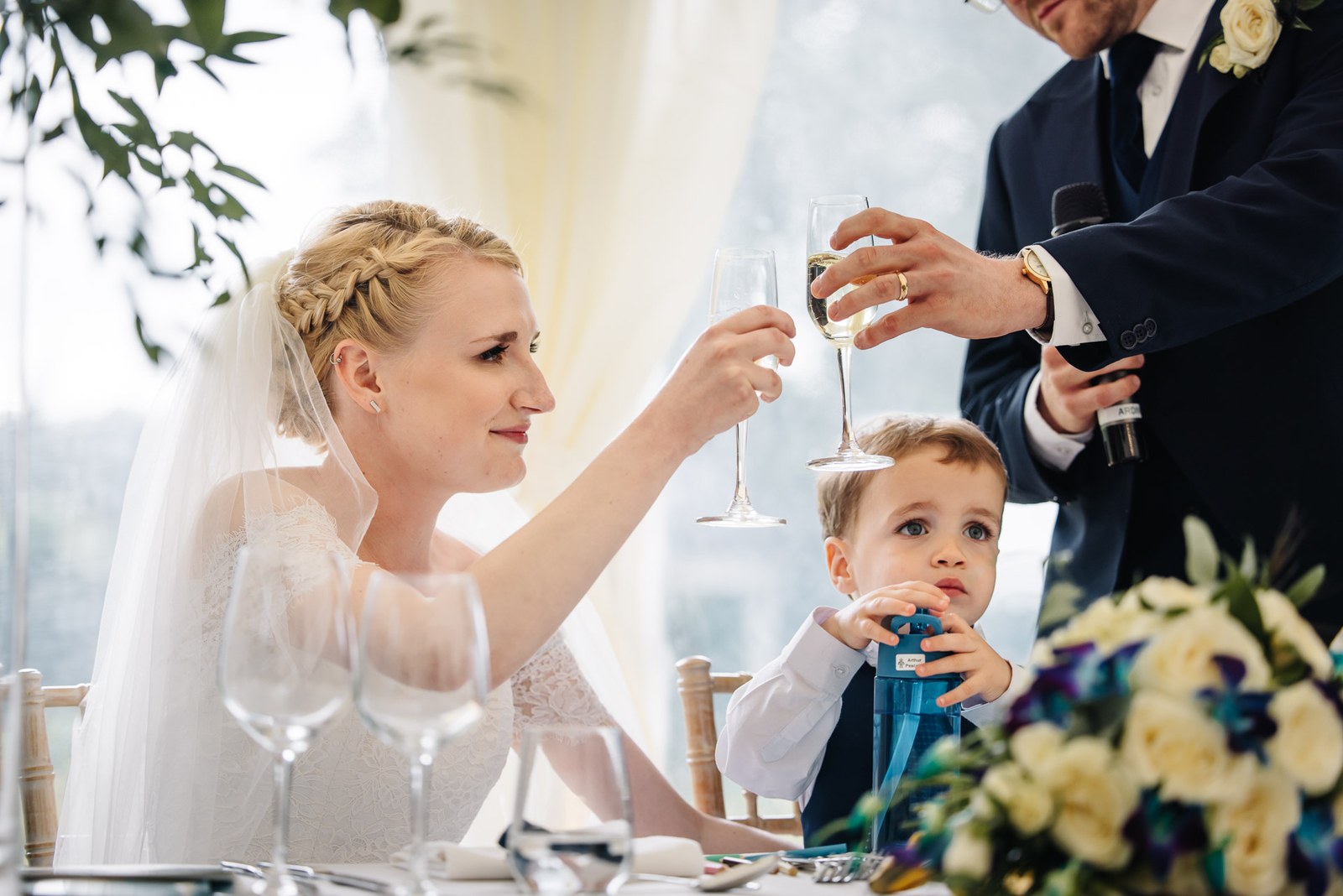 The bride raising a champagne toast beside the young page boy