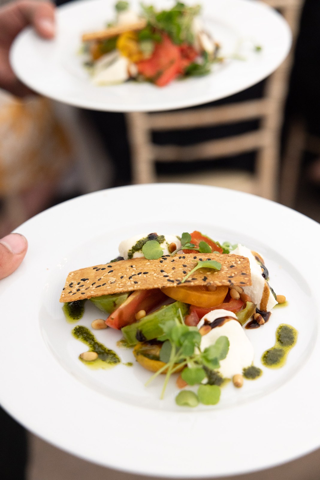 A plated tomato and mozzarella salad with pesto being carried to the tables