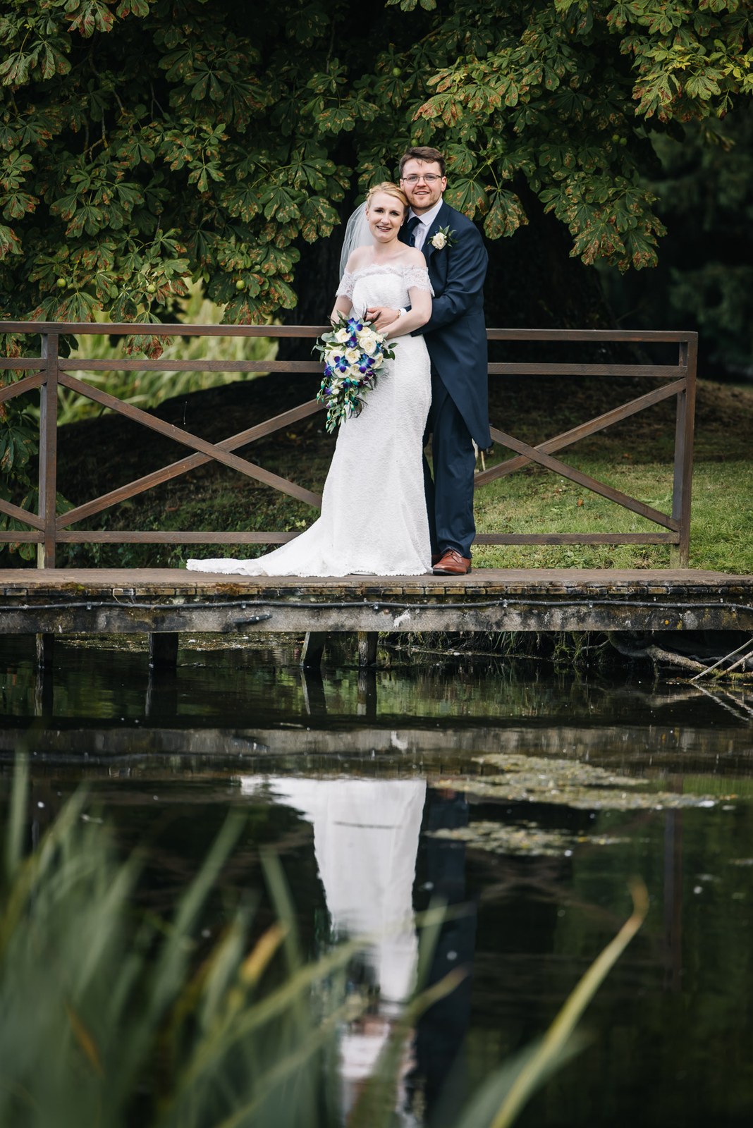 The couple on a wooden footbridge reflected in the still pond at Ardington House