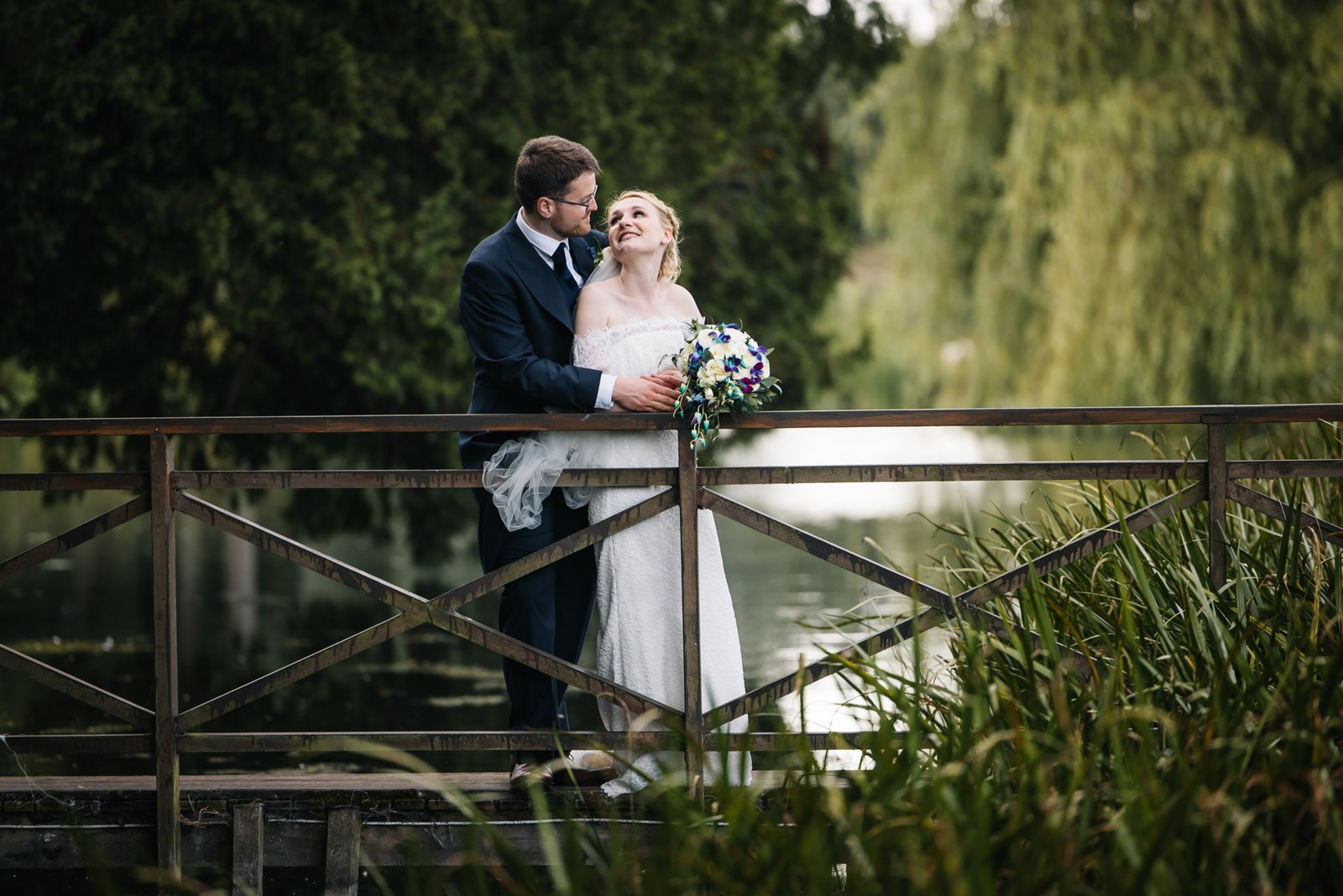Bride and groom embracing on the timber footbridge over the pond at Ardington House
