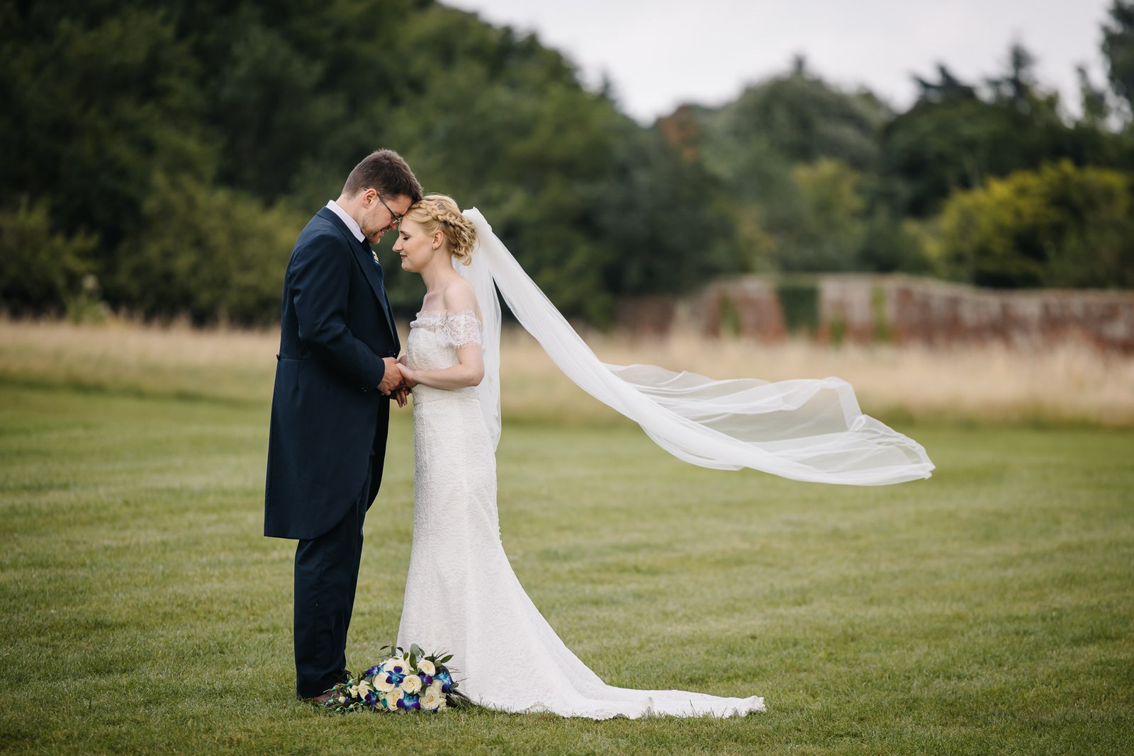 The bride's long veil catching the breeze as the couple embrace on the lawn
