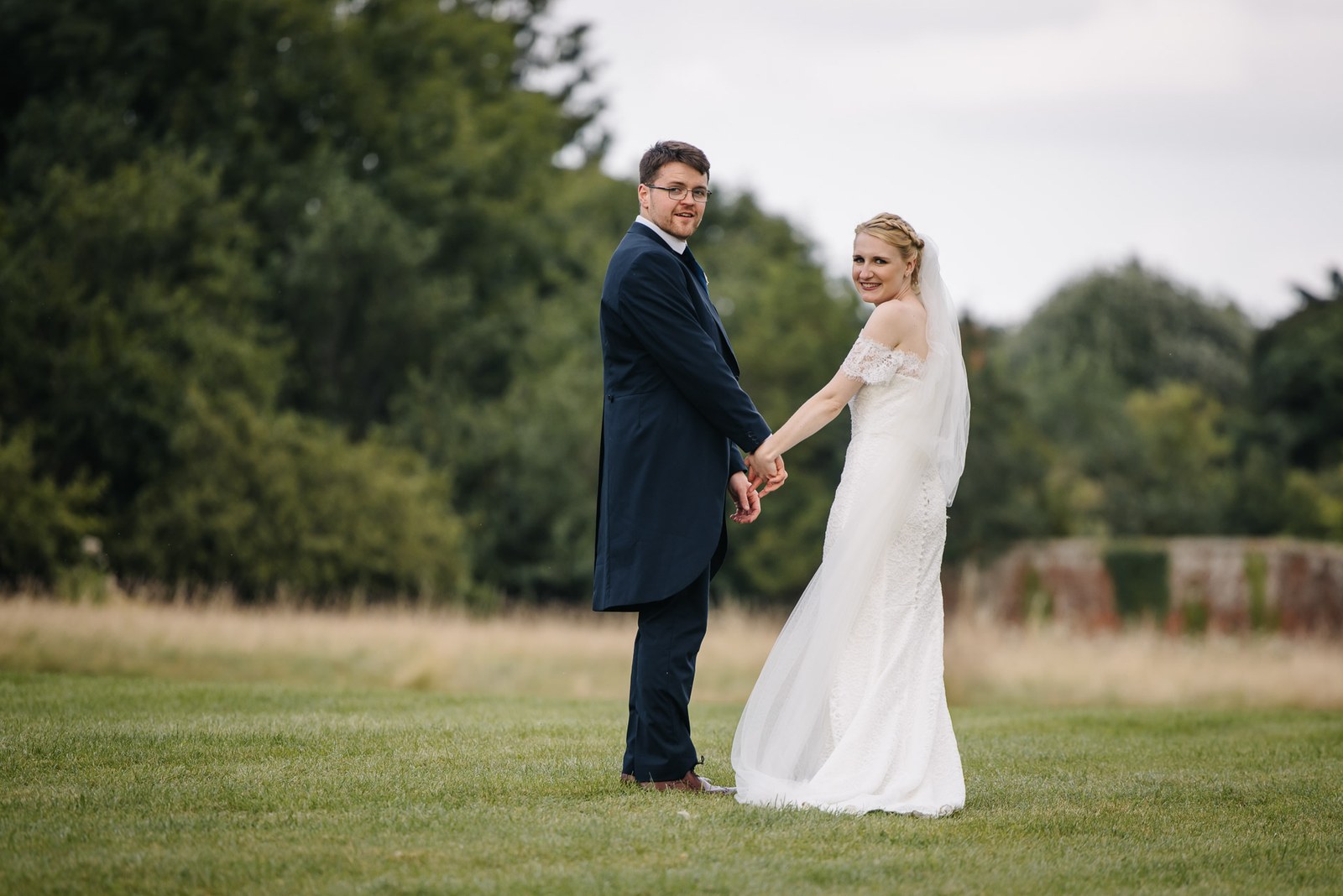 The couple hand in hand on the lawn, the groom glancing back