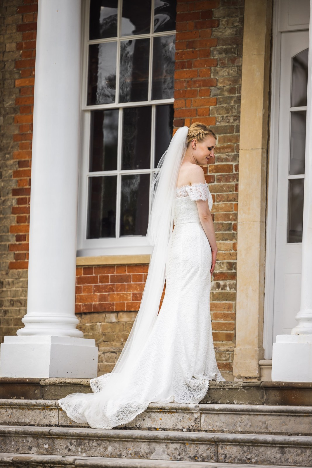 The bride with her long veil trailing beside the white portico of Ardington House