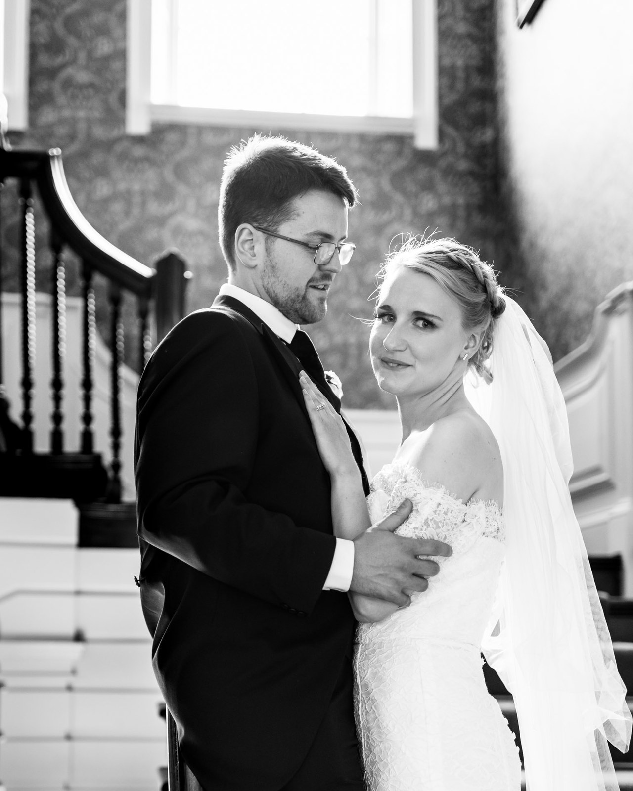 Black-and-white of the couple close together by an interior staircase