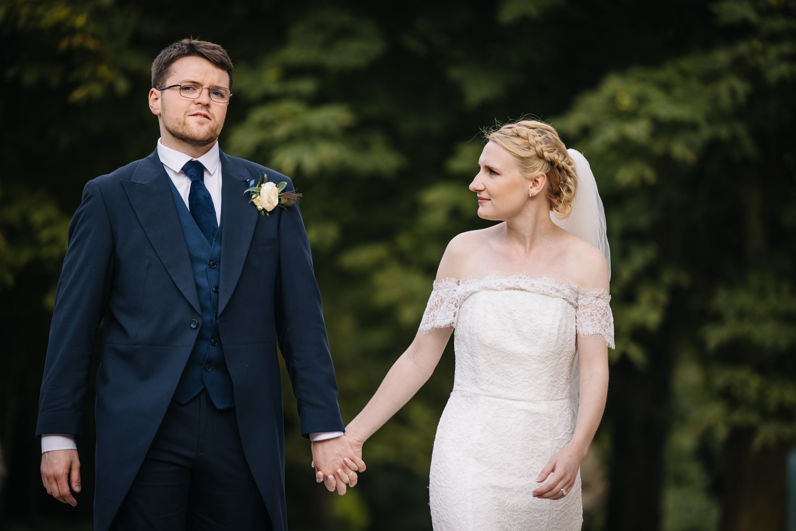 The couple holding hands on the lawn, the groom leading in the foreground