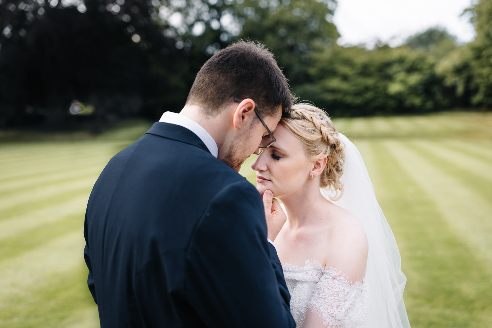 Bride and groom resting foreheads together on the mown lawn