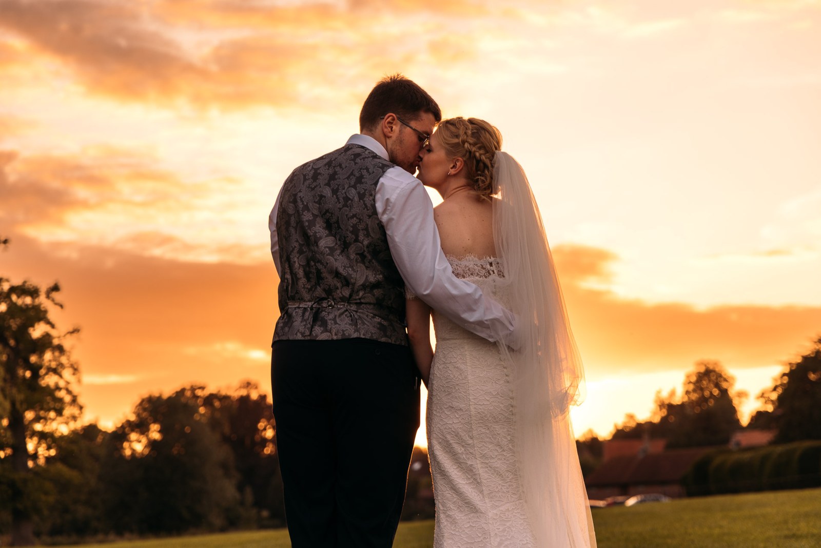 The couple kissing beneath a fiery orange sunset sky