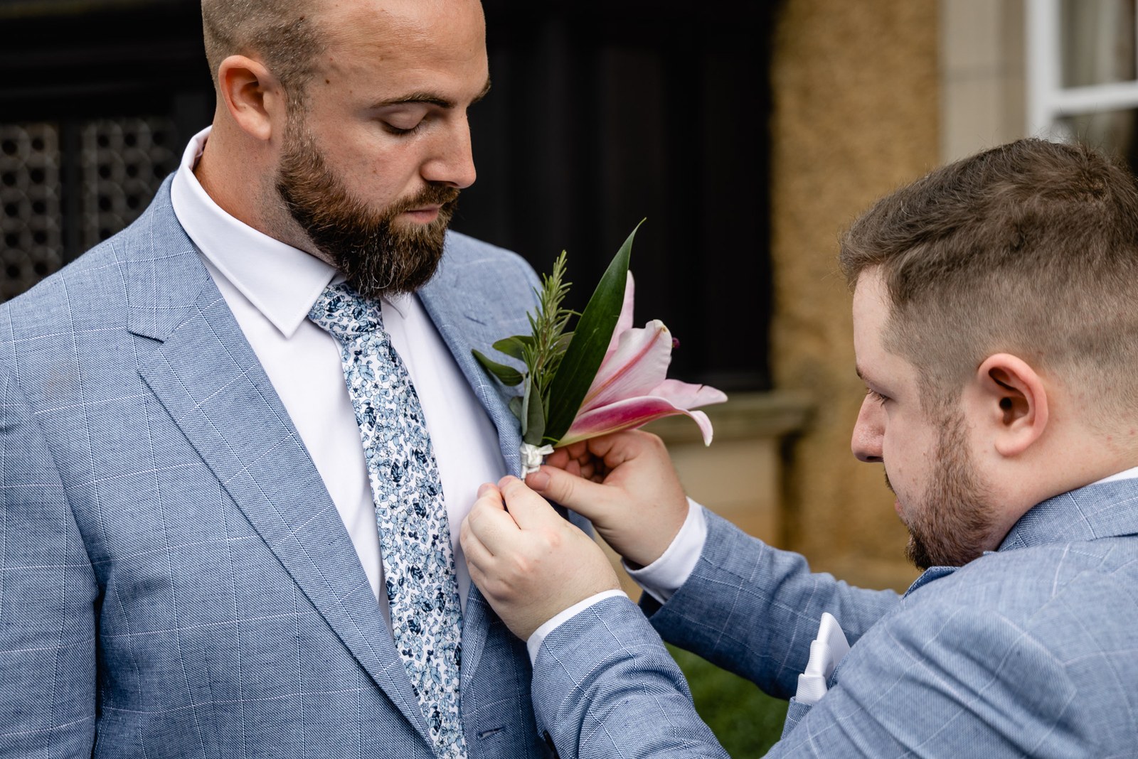 A groomsman pinning a pink lily buttonhole to the groom's lapel