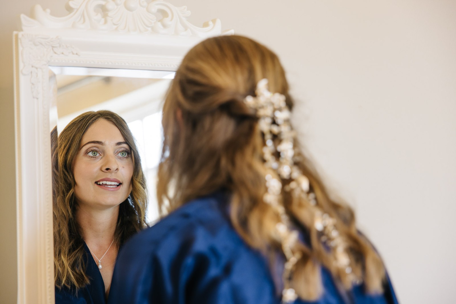 The bride studying her reflection and floral hairpiece in an ornate white mirror