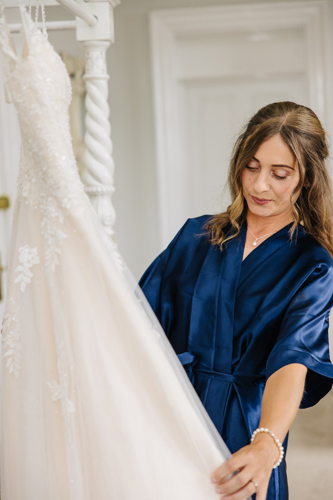 The bride in a navy robe admiring her lace wedding dress
