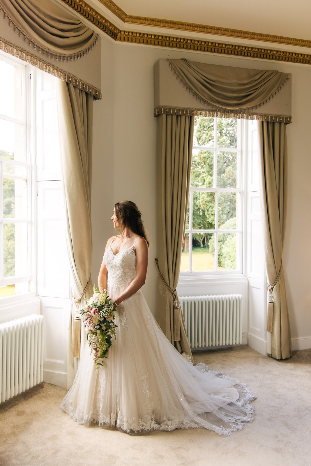 The bride framed by a grand bay window in a curtained room