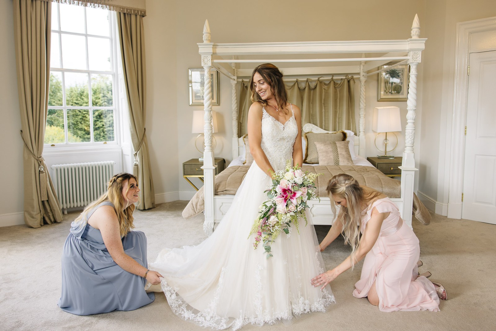 Two bridesmaids arranging the bride's train in the four-poster room