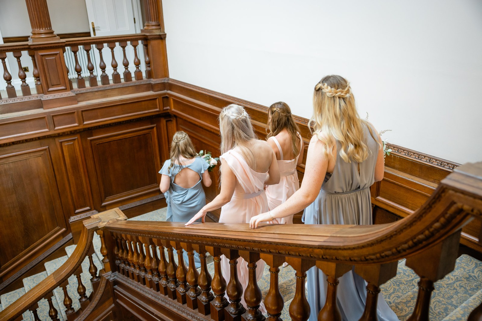 Bridesmaids and a flower girl descending the grand wooden staircase at Bourton Hall