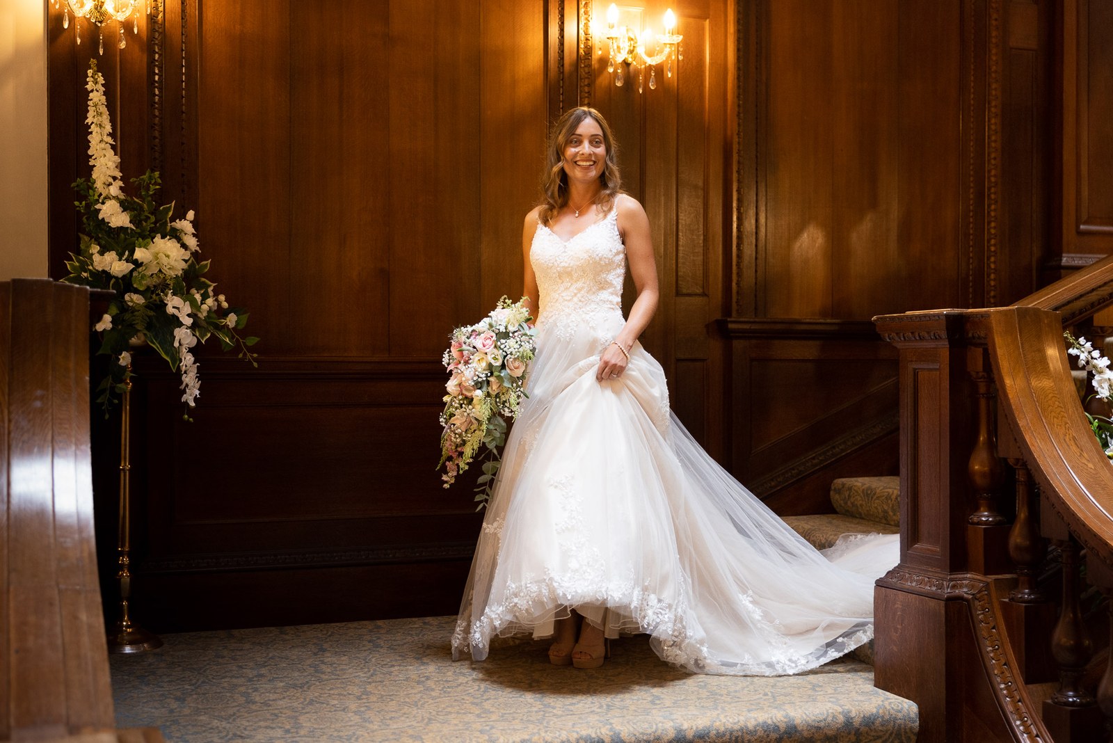 The bride coming down the grand carved staircase holding her bouquet