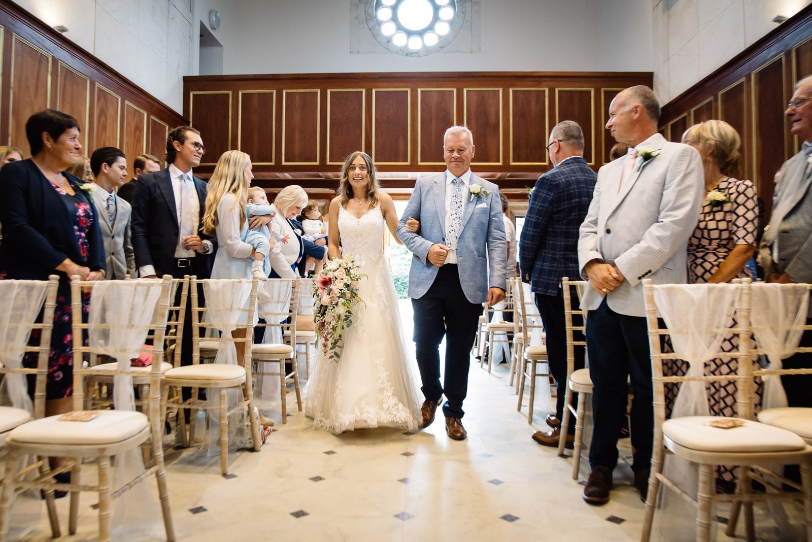 The bride walking down the aisle on her father's arm as guests stand