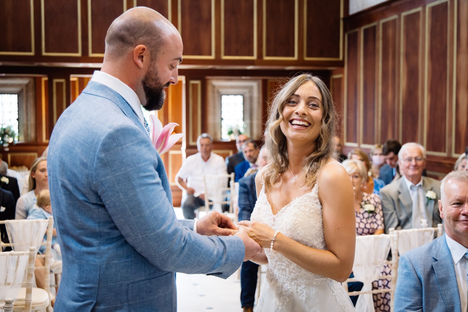The smiling bride exchanging rings with the groom as guests look on