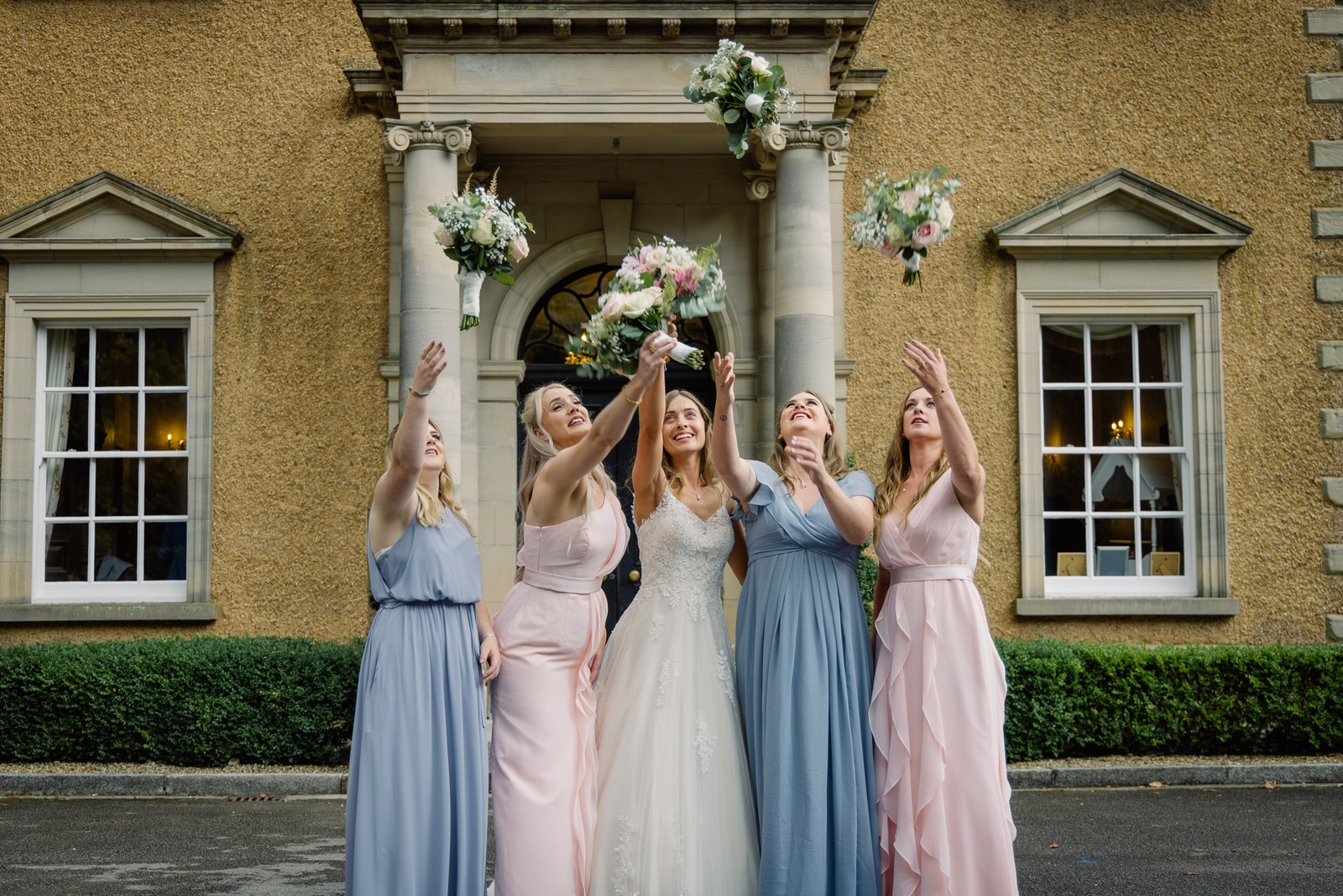 The bride and bridesmaids cheering before the columned entrance of Bourton Hall