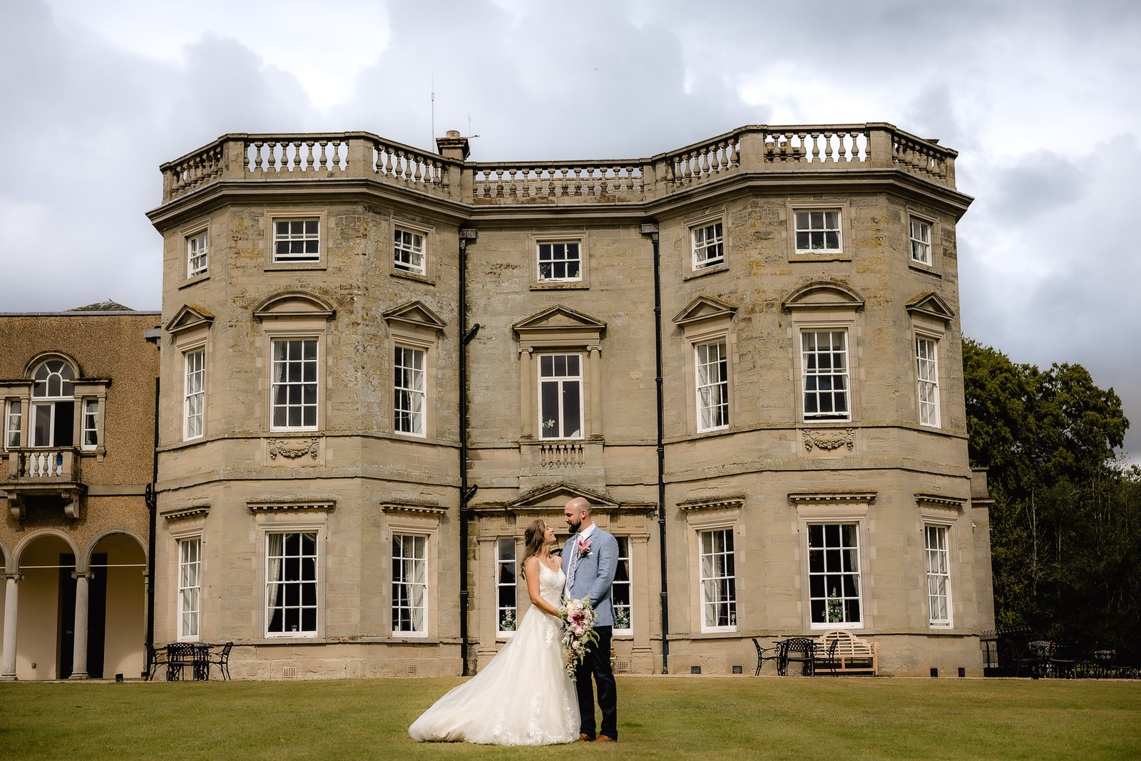 The couple dwarfed by the honey-stone facade of Bourton Hall