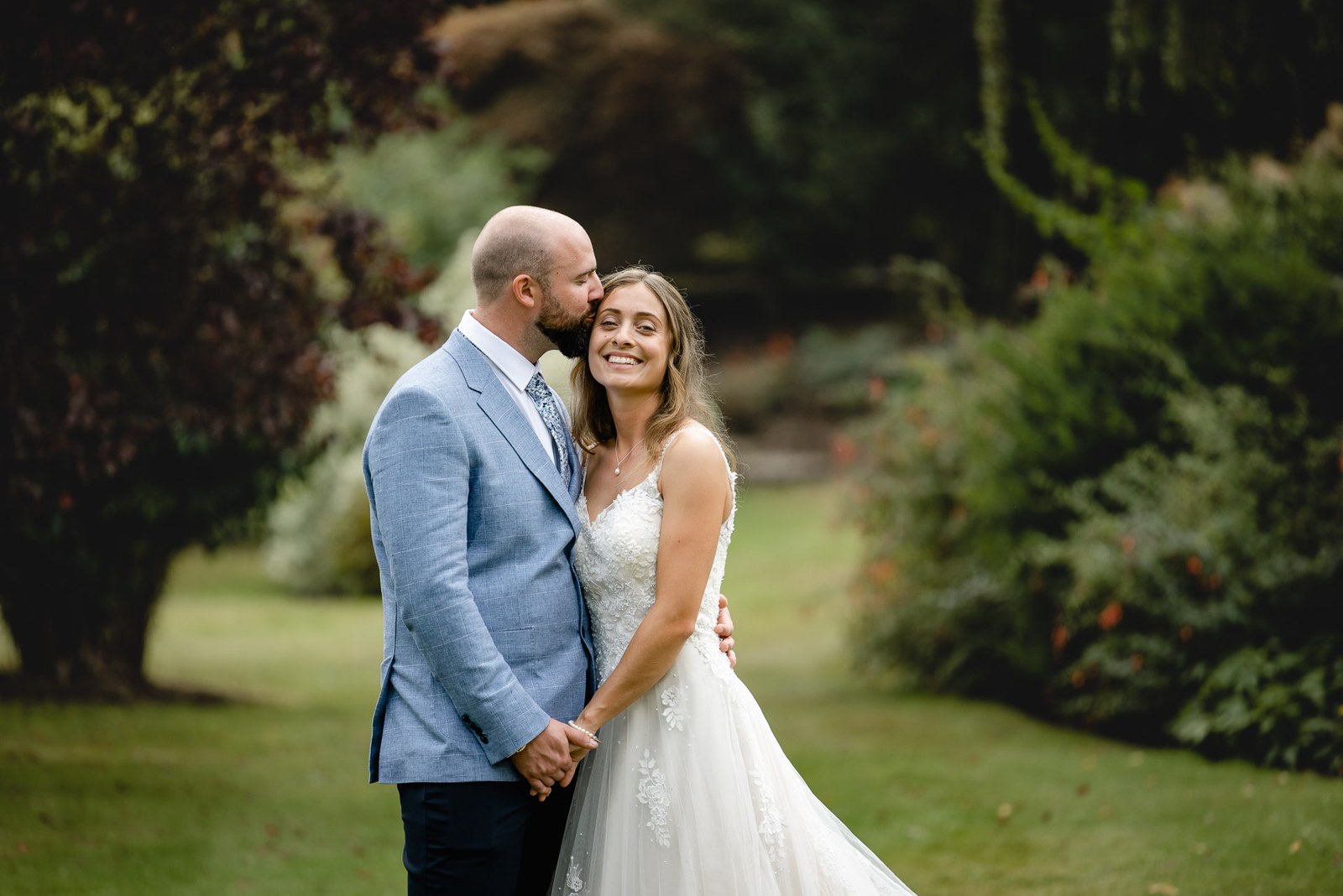 The groom kissing the bride's forehead on the lawn
