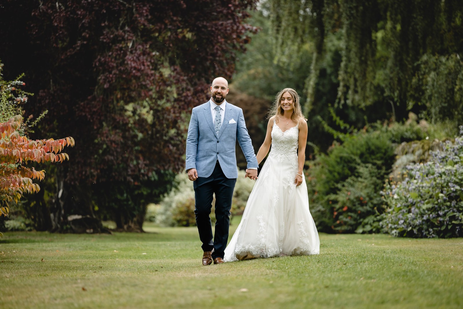 Bride and groom walking hand in hand across the grounds of Bourton Hall