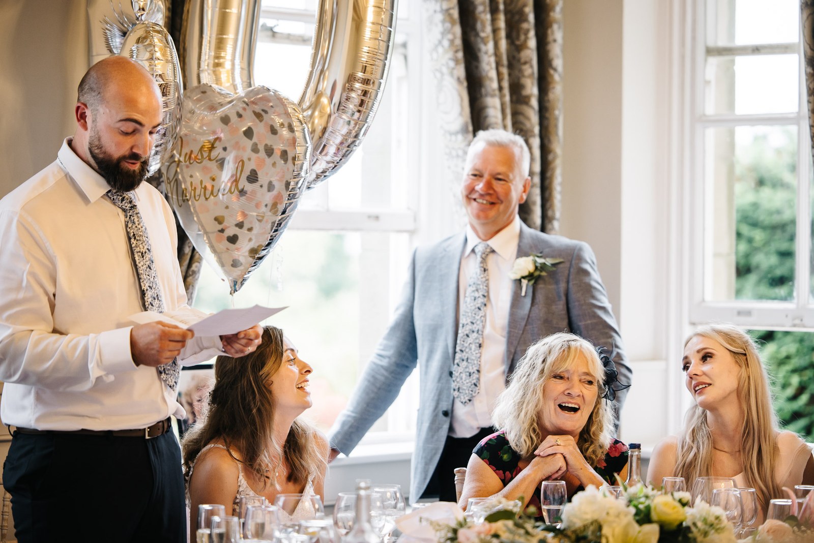 The groom delivering his speech beneath a 'Just Married' heart balloon