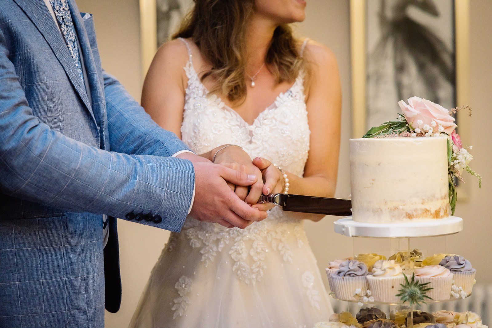 Close-up of the couple's hands slicing the cake above a tier of cupcakes