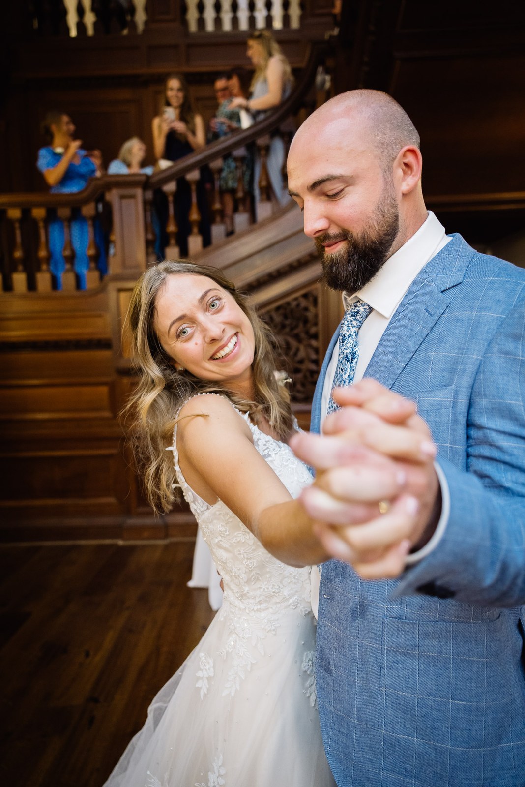 The first dance on the wooden floor as guests watch from the staircase