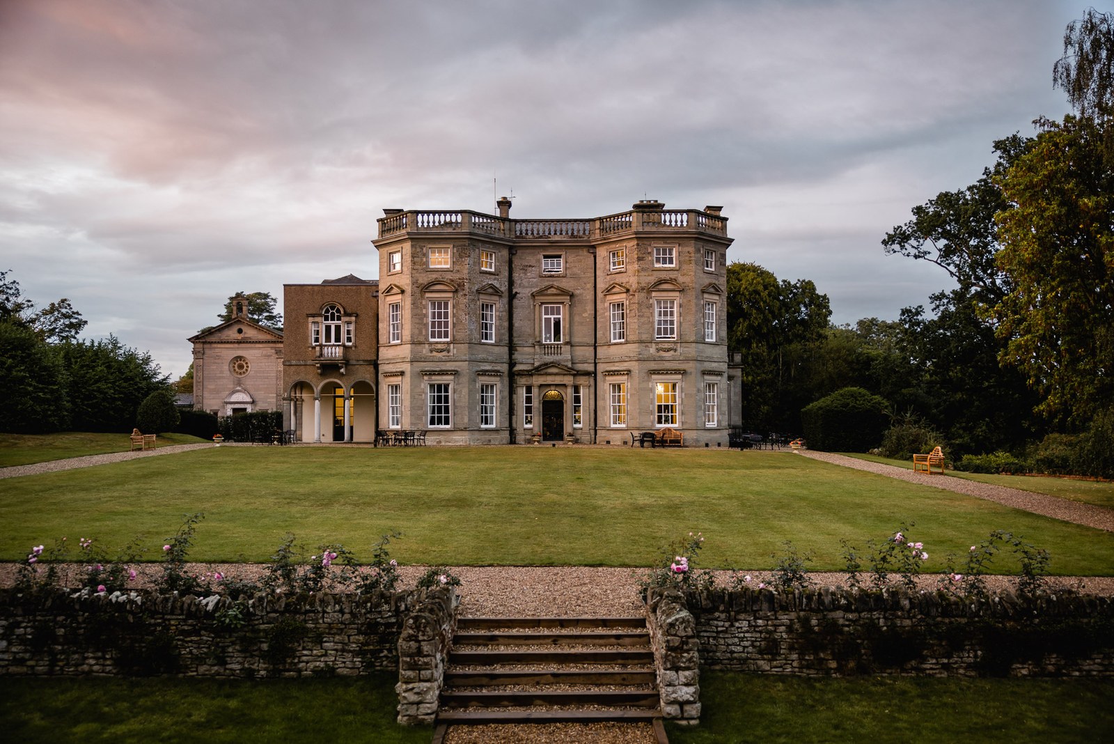 The honey-stone facade of Bourton Hall above its lawns at dusk