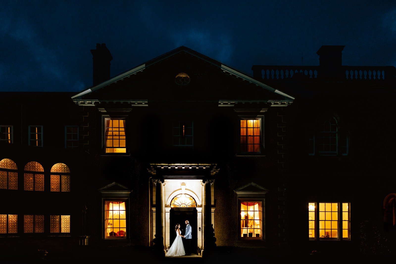 Bourton Hall glowing at night with the couple silhouetted in the doorway