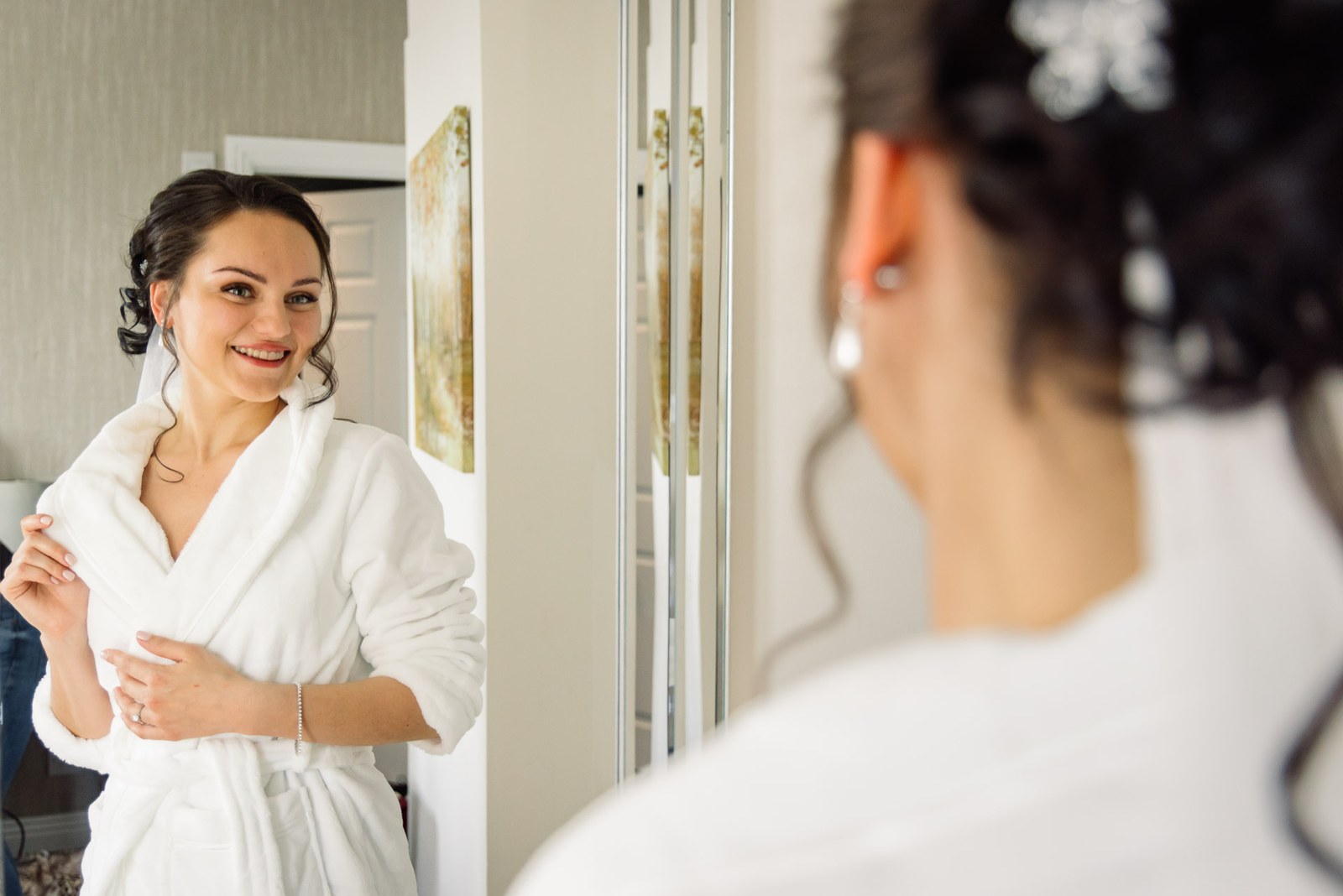 The bride in a white robe checking her reflection in the mirror before dressing