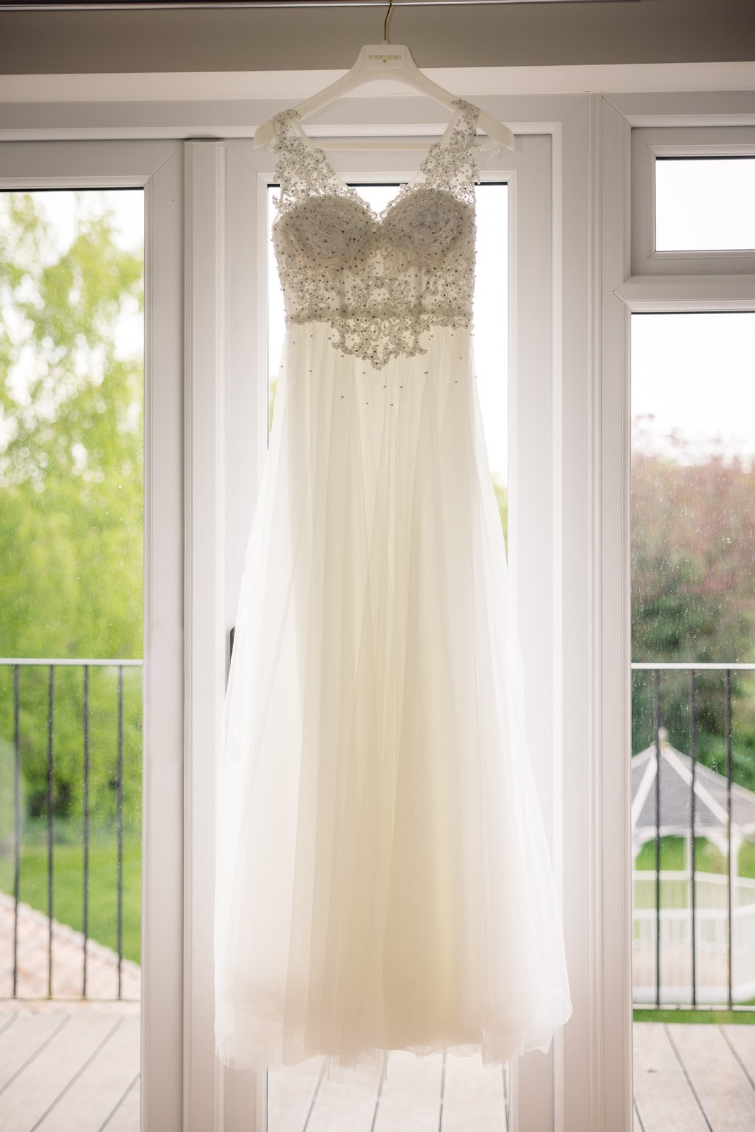 The beaded wedding gown hanging in a bright balcony doorway