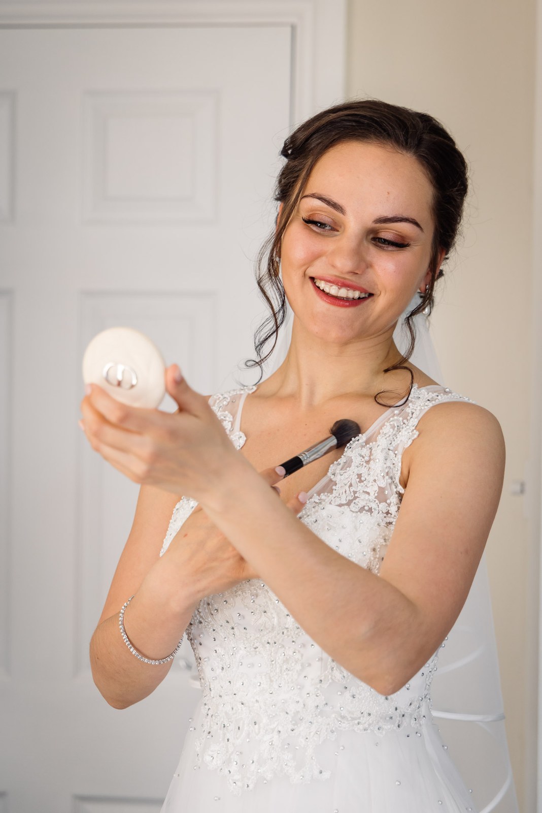 The bride smiling as she applies makeup with a compact mirror