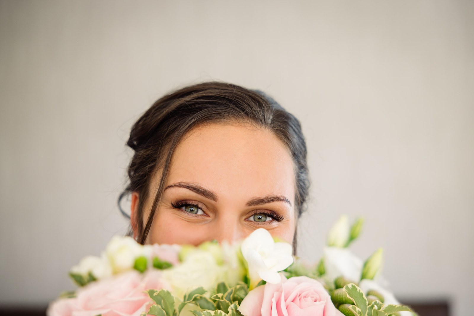 The bride's eyes peeking over her pink and white bouquet
