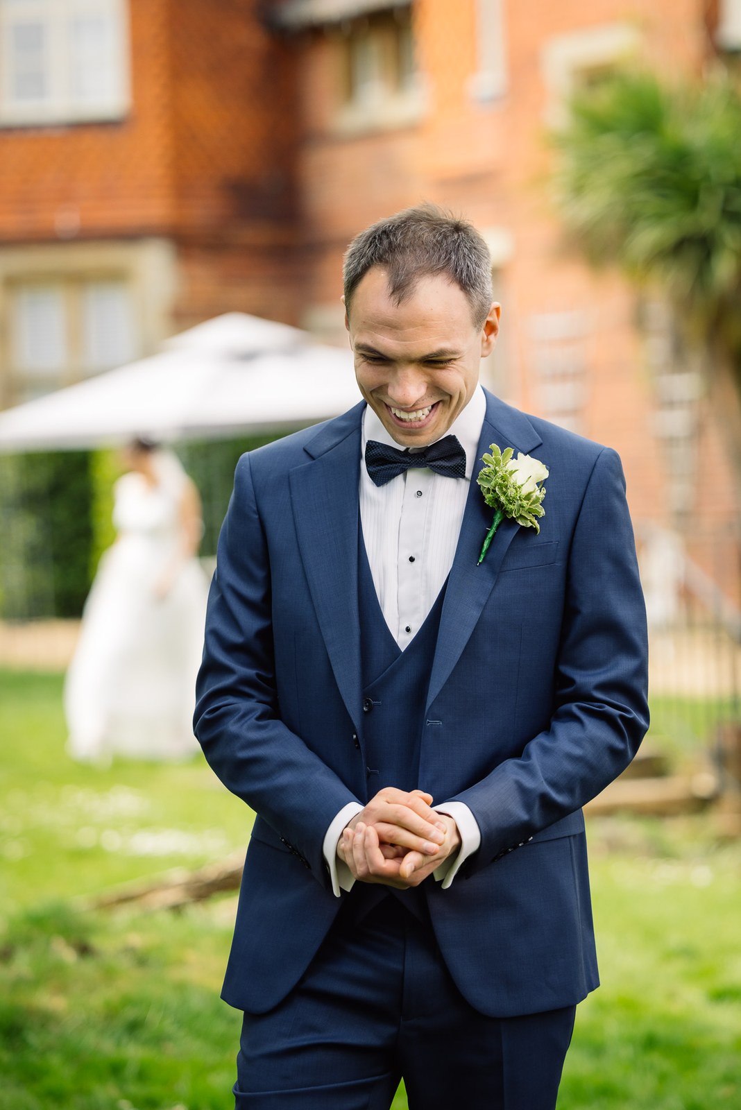 The groom waiting on the lawn as the bride approaches for their first look