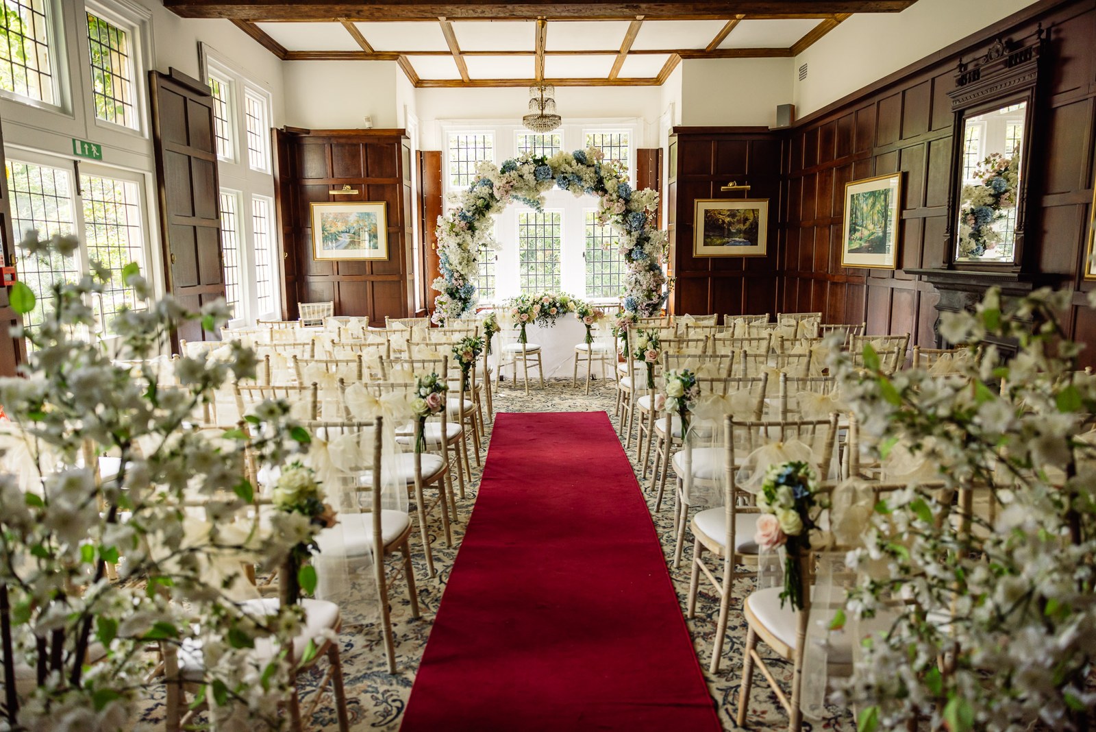The wood-panelled ceremony room at Cantley House Hotel with a red aisle and floral arch