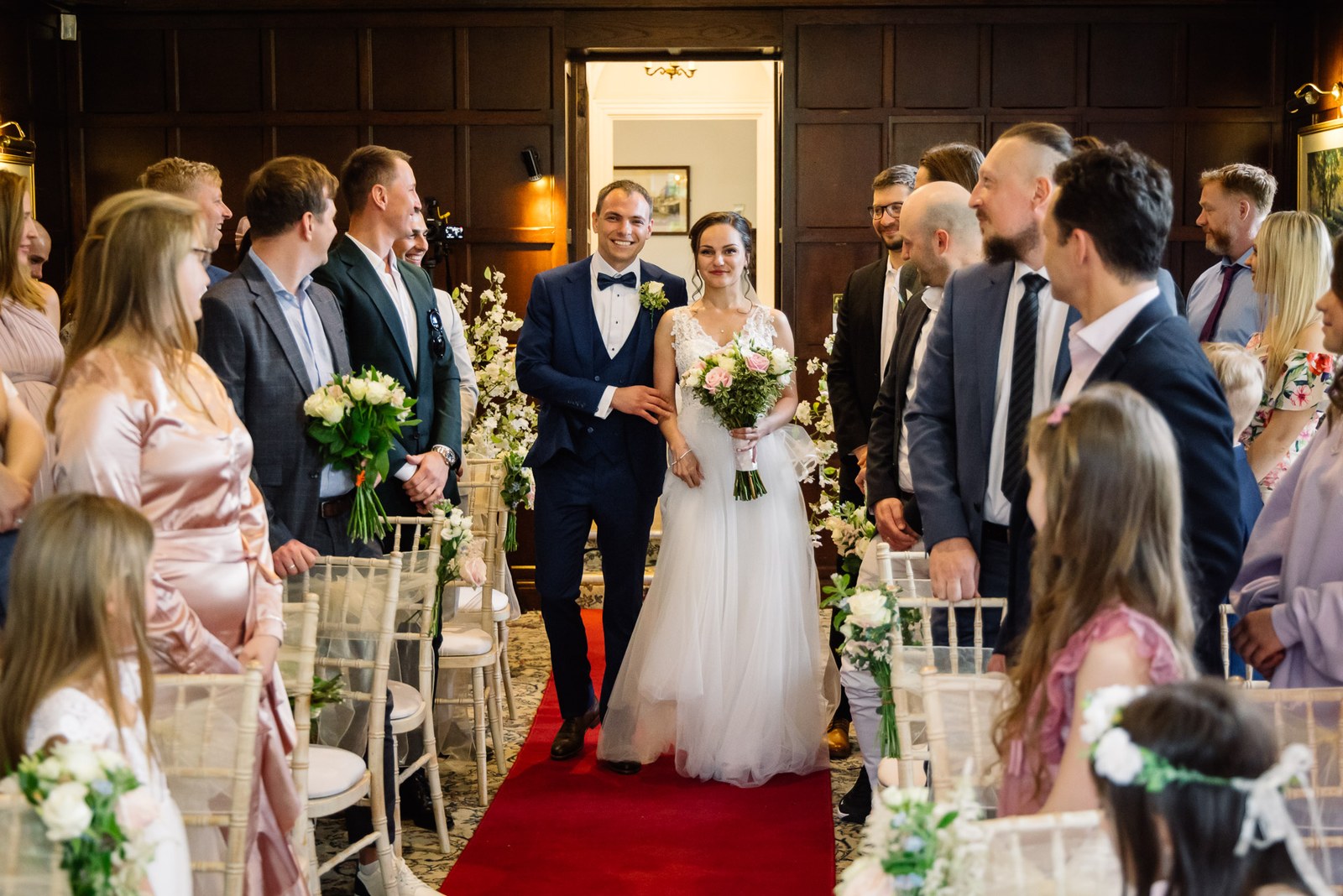 Bride and groom walking the red-carpet aisle as guests stand