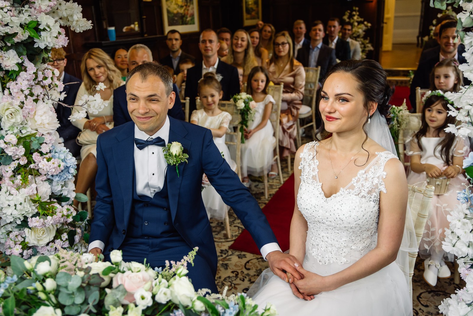 The couple seated at the ceremony beneath a blossom arch