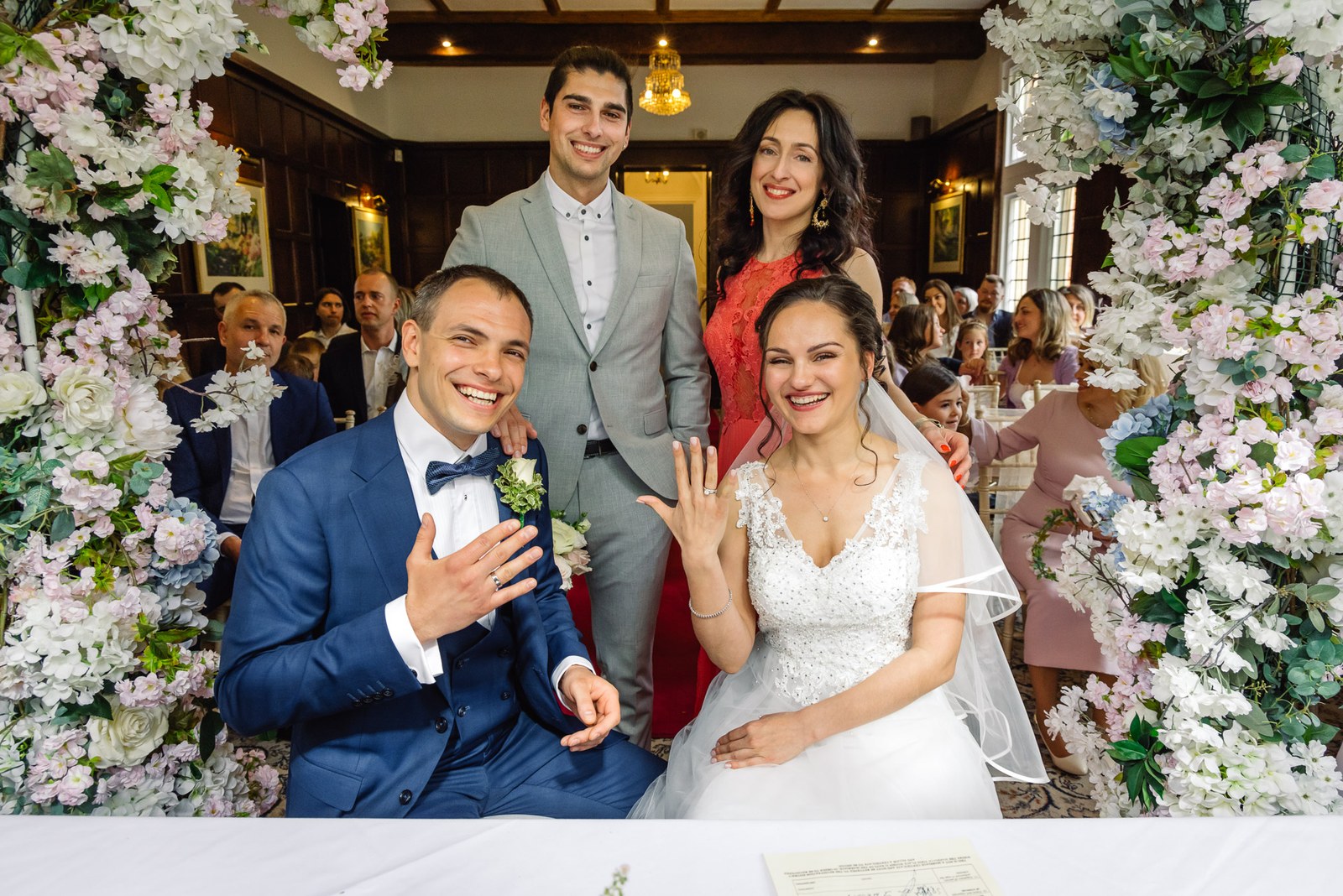 The seated couple showing their rings with witnesses behind