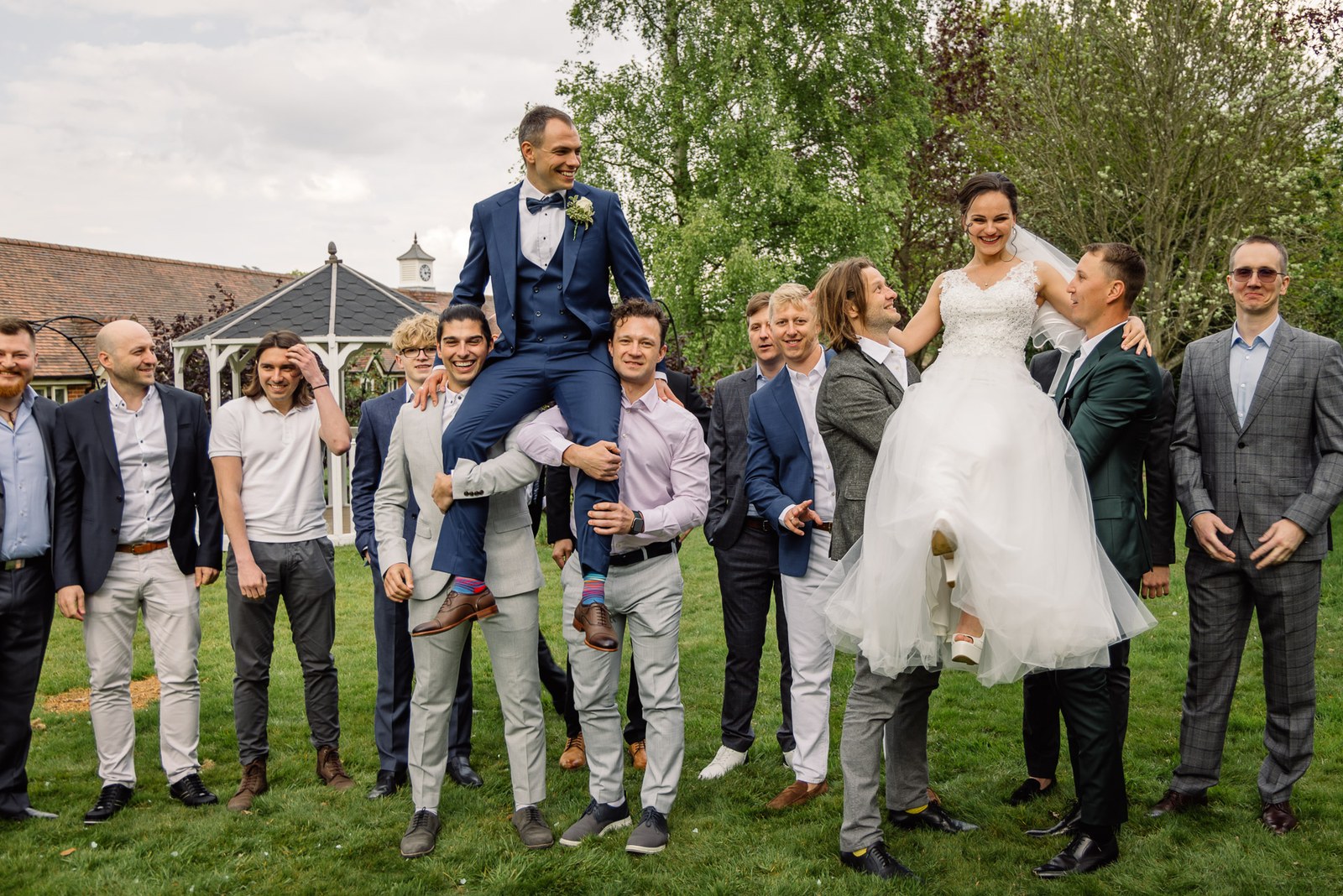 The groom hoisted on his groomsmen's shoulders on the lawn