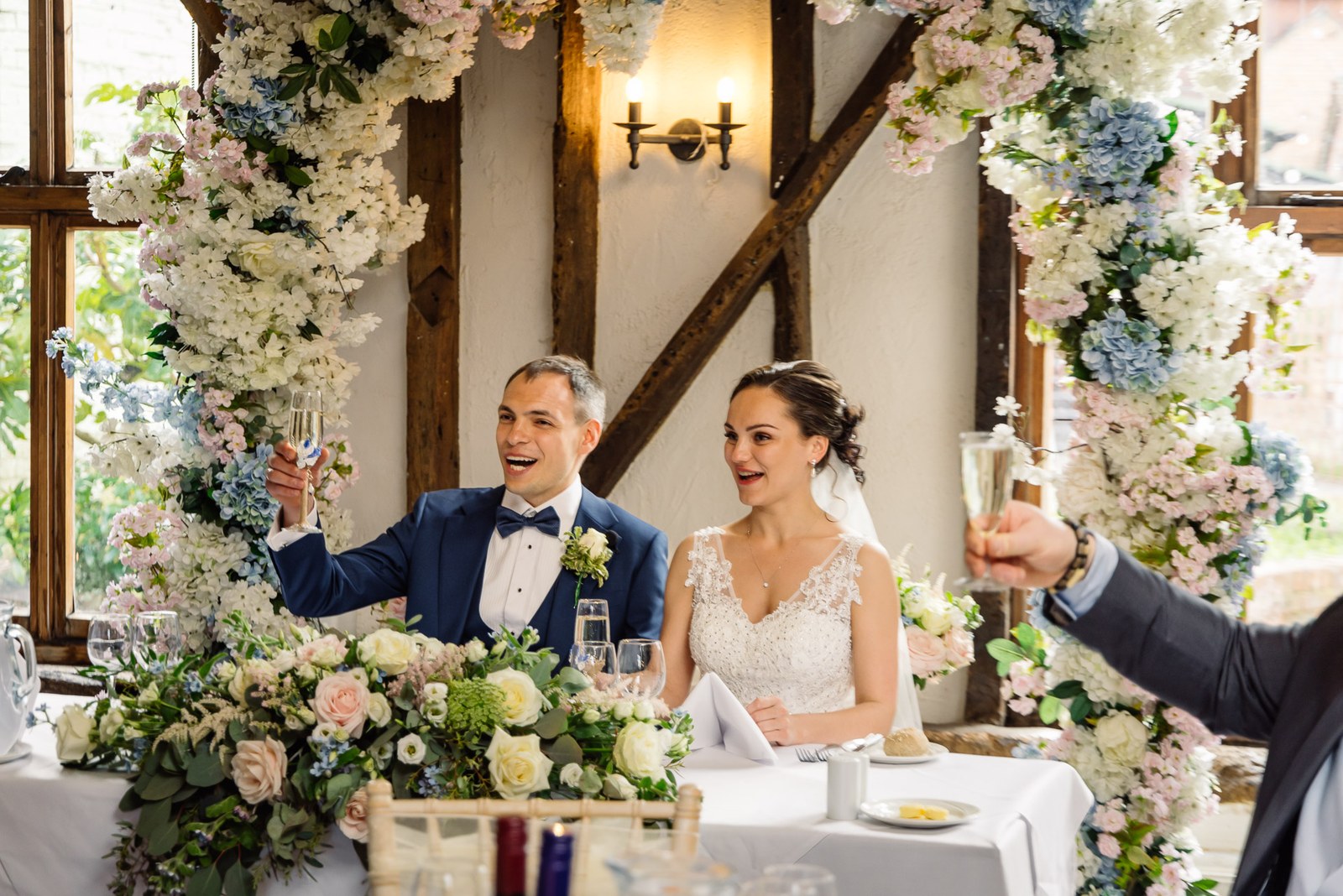 The couple raising a toast at the top table beneath a floral arch