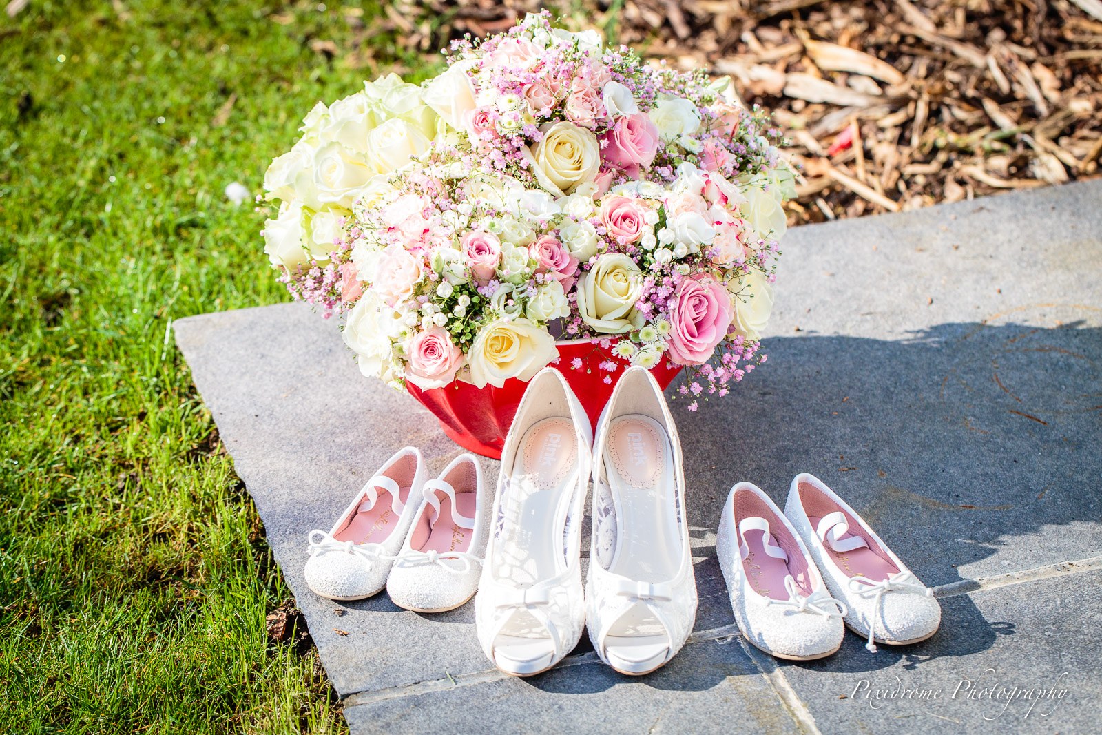 The bridal bouquet of pink and white roses beside the wedding shoes on the ground