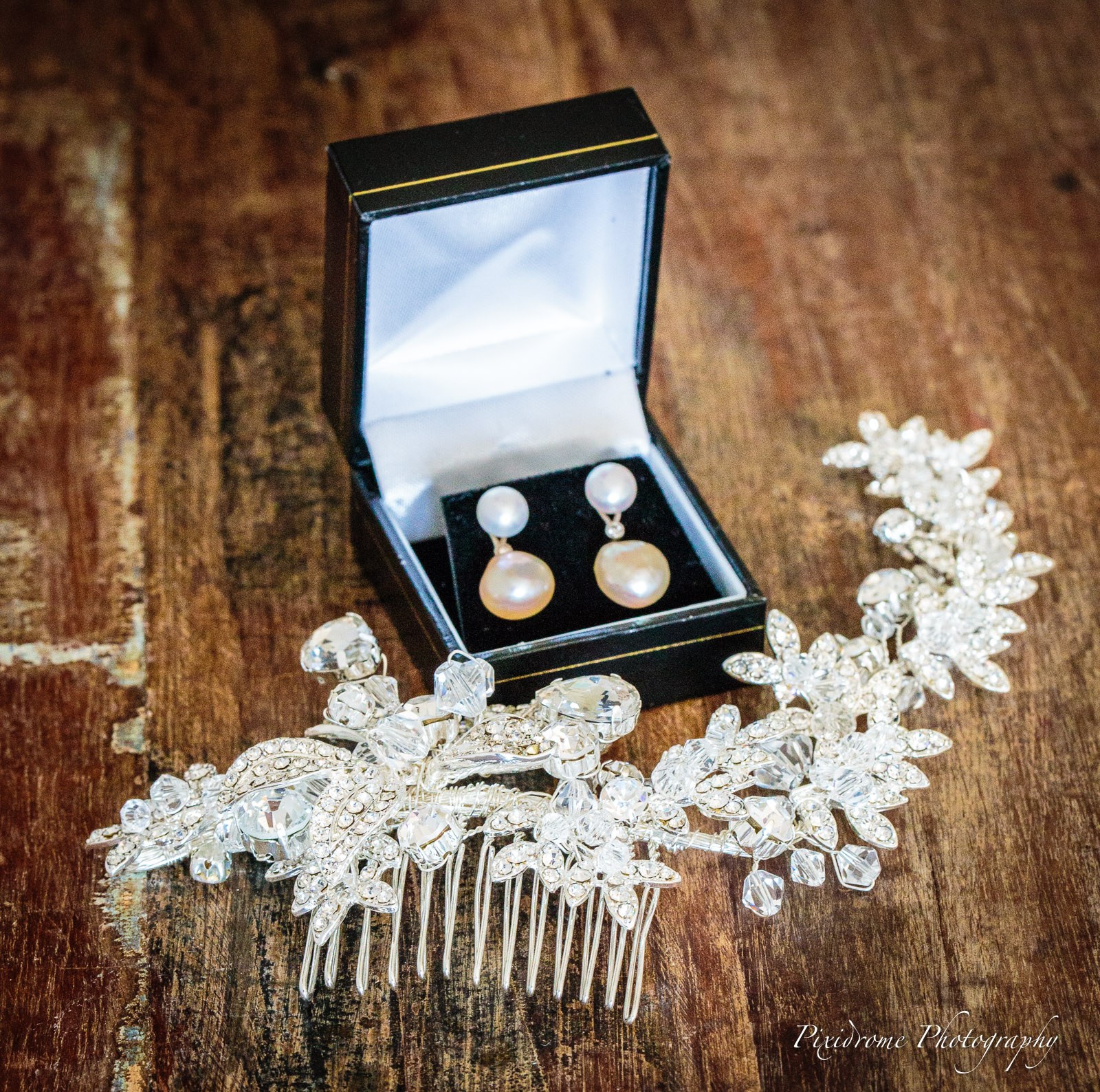 Pearl drop earrings in a box beside a crystal hair comb on rustic wood